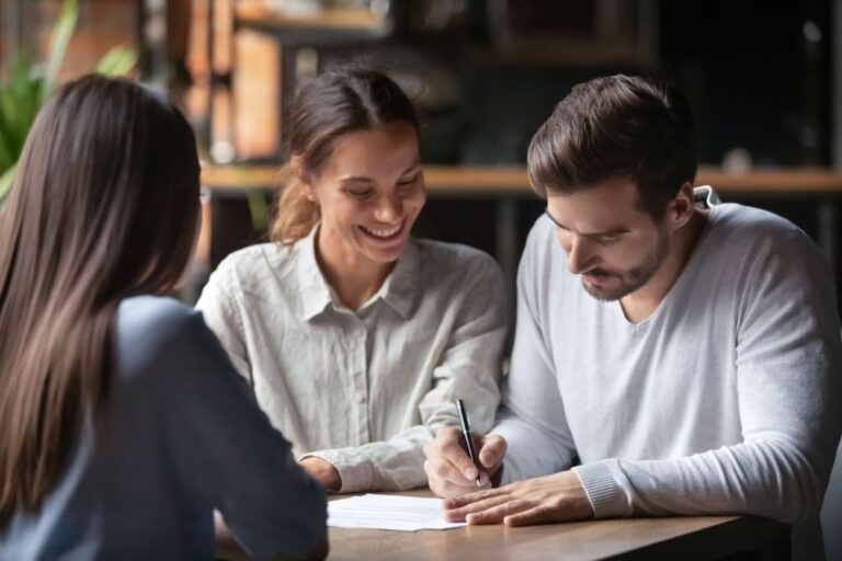 Three people sign a commercial roofing contract in office setting.